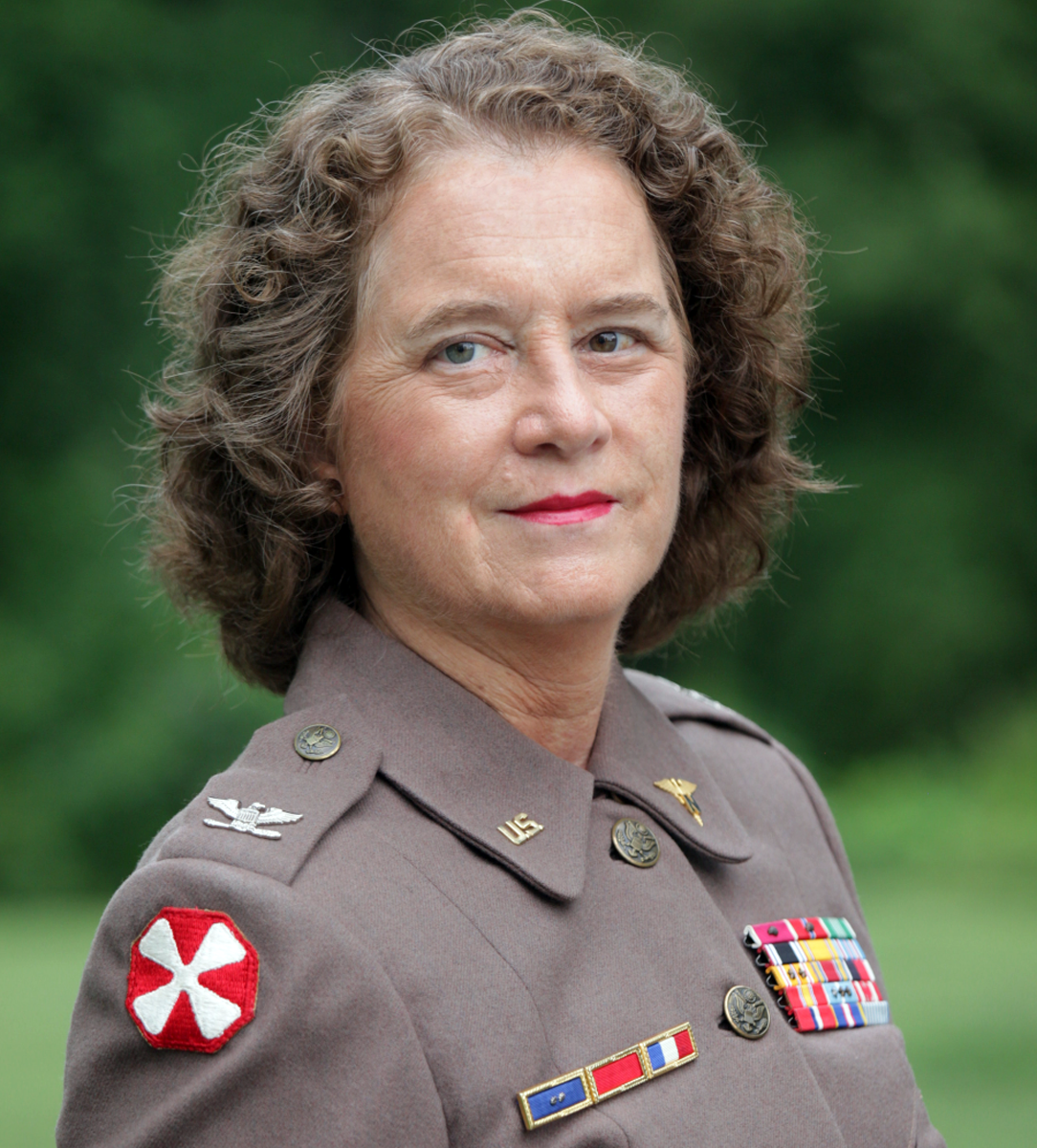 Becky Park as Col. Ruby Bradley, with brownish-red hair wearing dress nurse's Army uniform from the Korean War era
